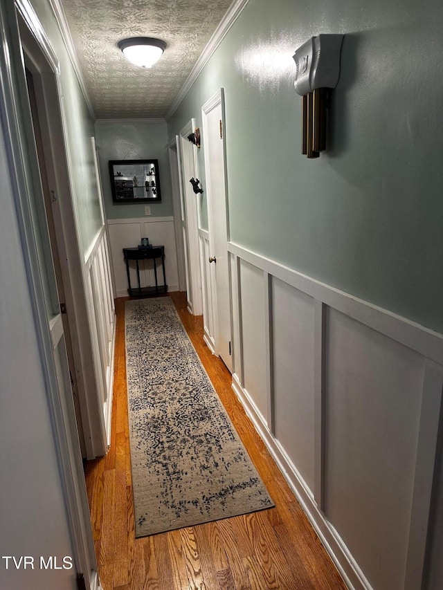 hallway featuring light hardwood / wood-style floors, a textured ceiling, and ornamental molding