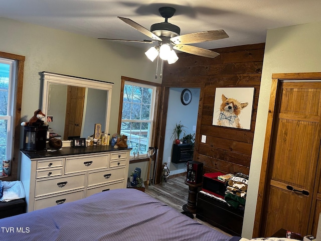 bedroom with ceiling fan, wood walls, and multiple windows