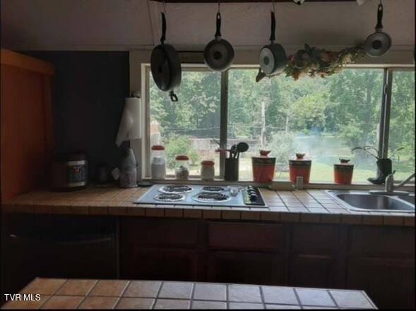 kitchen featuring dark brown cabinetry, gas stovetop, tile counters, and sink