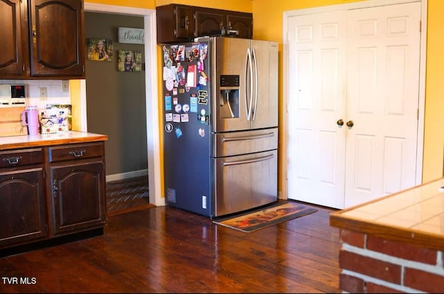 kitchen with backsplash, dark brown cabinets, dark wood-type flooring, and stainless steel refrigerator with ice dispenser