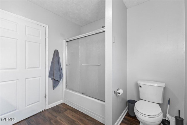 bathroom with hardwood / wood-style floors, a textured ceiling, toilet, and enclosed tub / shower combo