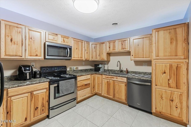 kitchen with light brown cabinetry, dark stone counters, a textured ceiling, stainless steel appliances, and sink