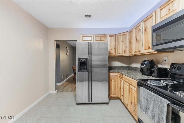 kitchen featuring light brown cabinetry, a textured ceiling, stainless steel appliances, and light tile patterned flooring