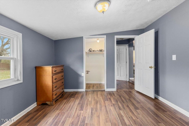 unfurnished bedroom with dark hardwood / wood-style flooring, a walk in closet, a textured ceiling, a closet, and lofted ceiling