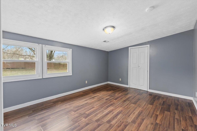 empty room featuring a textured ceiling, dark wood-type flooring, and lofted ceiling