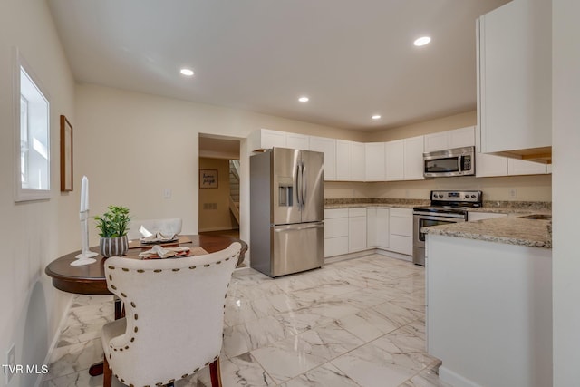 kitchen with stainless steel appliances, white cabinetry, light stone counters, and kitchen peninsula