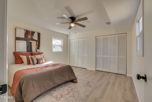 bedroom featuring ceiling fan, a textured ceiling, light hardwood / wood-style floors, and multiple closets