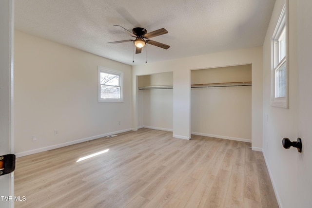 unfurnished bedroom with ceiling fan, two closets, light hardwood / wood-style flooring, and a textured ceiling