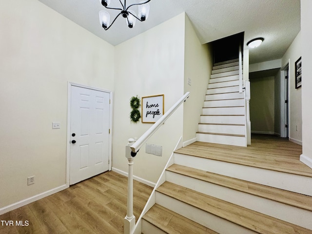 stairs with wood-type flooring, a notable chandelier, and a textured ceiling