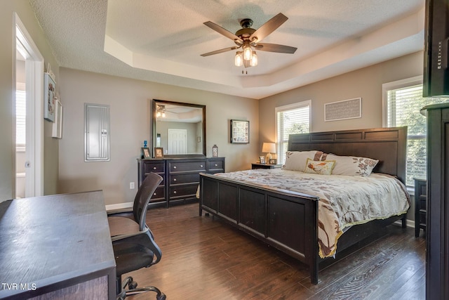 bedroom with ensuite bath, ceiling fan, electric panel, dark hardwood / wood-style flooring, and a raised ceiling