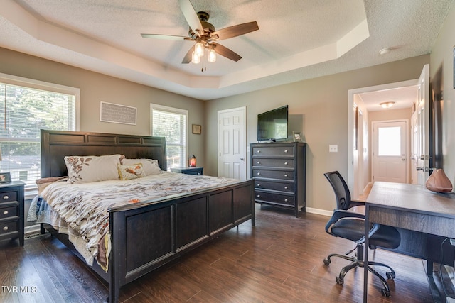 bedroom featuring a raised ceiling, dark hardwood / wood-style flooring, a textured ceiling, and ceiling fan