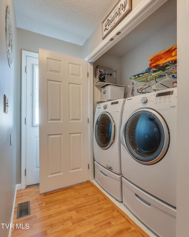 washroom featuring washing machine and dryer, a textured ceiling, and light hardwood / wood-style floors