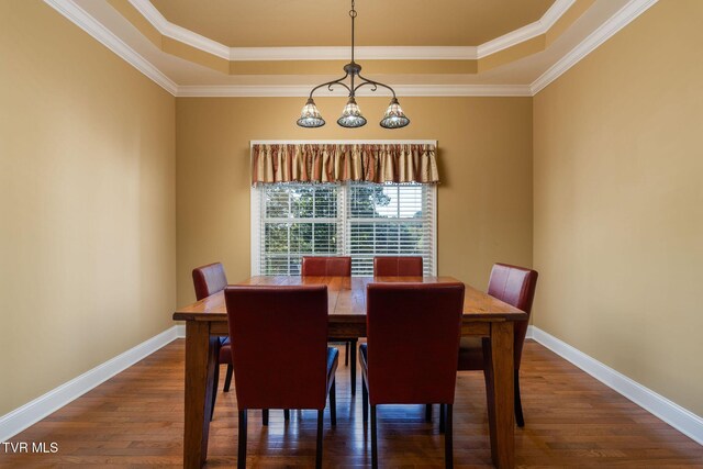 dining area with a tray ceiling, crown molding, and dark wood-type flooring