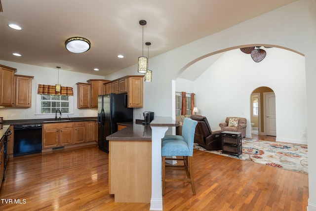 kitchen featuring black appliances, a breakfast bar, wood-type flooring, and kitchen peninsula