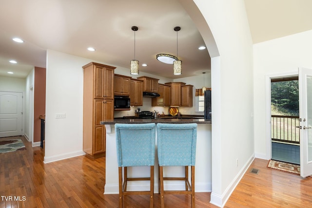 kitchen with decorative light fixtures, light hardwood / wood-style floors, a kitchen breakfast bar, and kitchen peninsula