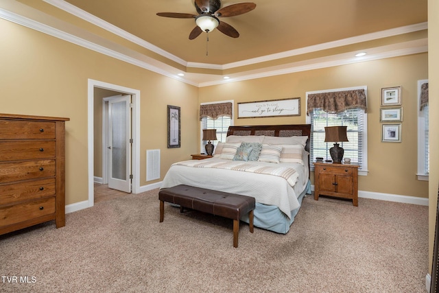 carpeted bedroom with a tray ceiling, multiple windows, ceiling fan, and crown molding