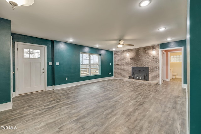 unfurnished living room featuring hardwood / wood-style floors, a wood stove, ceiling fan, and plenty of natural light