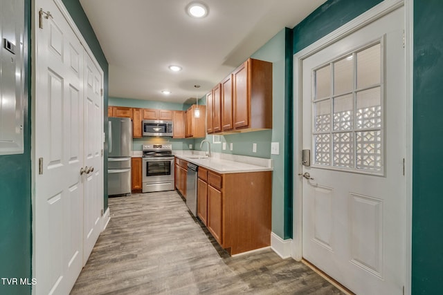 kitchen featuring sink, light hardwood / wood-style flooring, decorative light fixtures, and appliances with stainless steel finishes