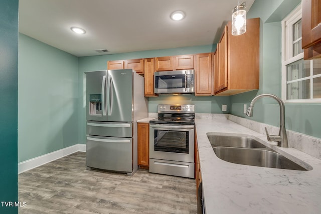 kitchen featuring hanging light fixtures, sink, stainless steel appliances, and light hardwood / wood-style floors