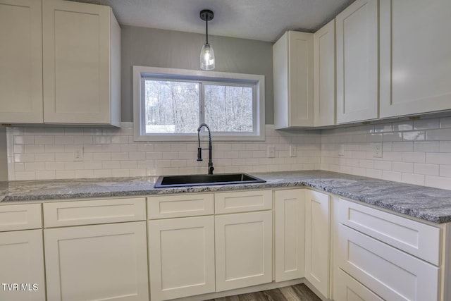 kitchen featuring backsplash, sink, white cabinets, and hanging light fixtures