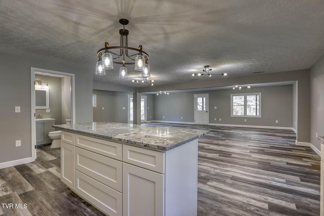 kitchen featuring dark wood-type flooring, light stone countertops, a textured ceiling, decorative light fixtures, and white cabinetry