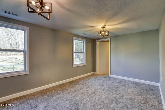 spare room featuring carpet floors, a textured ceiling, a wealth of natural light, and a chandelier