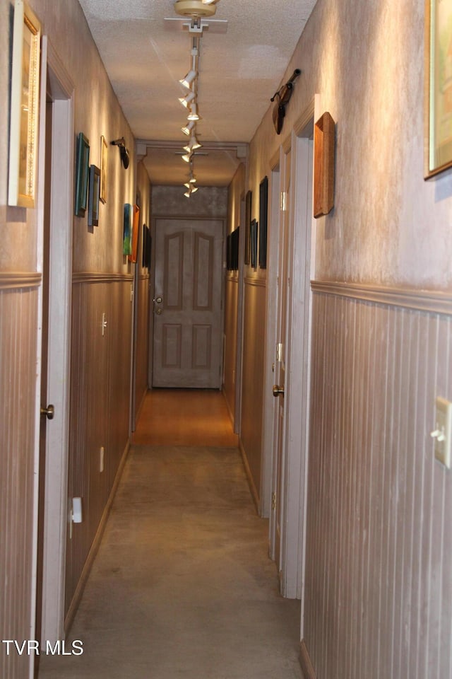 corridor featuring a textured ceiling, rail lighting, and wooden walls