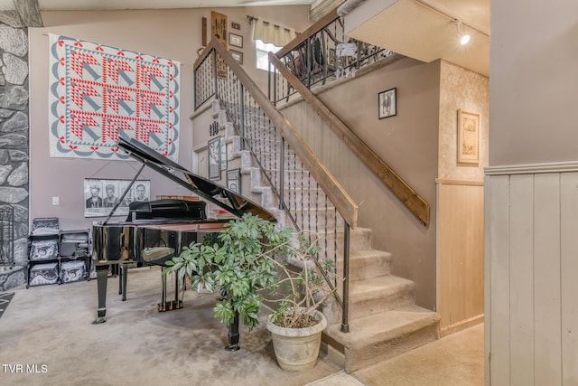 stairway featuring a high ceiling, rail lighting, and wainscoting