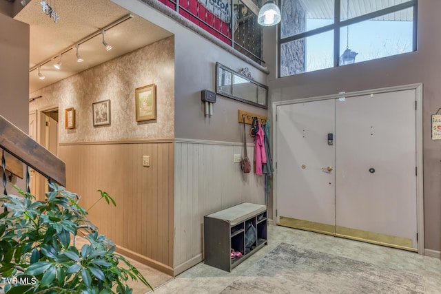 foyer entrance with rail lighting, a wainscoted wall, wood walls, and a towering ceiling