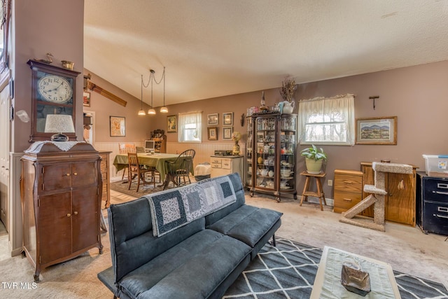 living room with vaulted ceiling, carpet flooring, wainscoting, and a textured ceiling