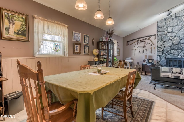 dining room with a stone fireplace, wainscoting, and vaulted ceiling