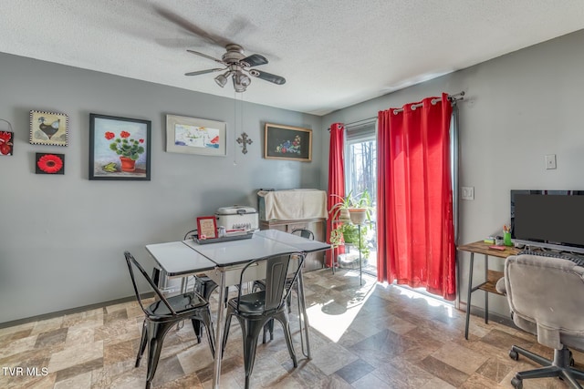 dining space featuring baseboards, a textured ceiling, stone finish flooring, and a ceiling fan