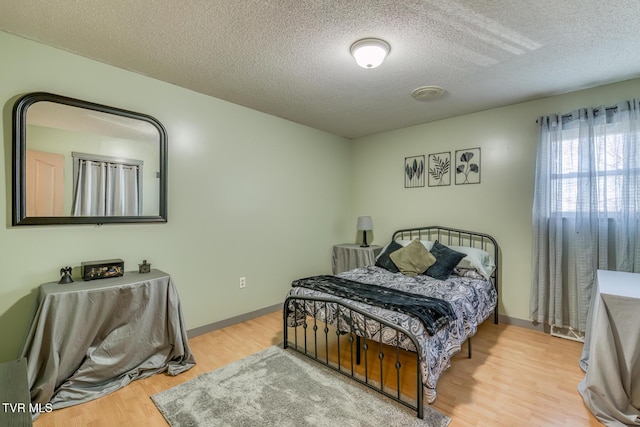 bedroom featuring baseboards, a textured ceiling, and wood finished floors
