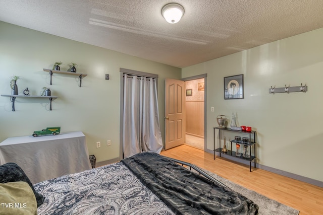 bedroom featuring light wood-type flooring, baseboards, and a textured ceiling
