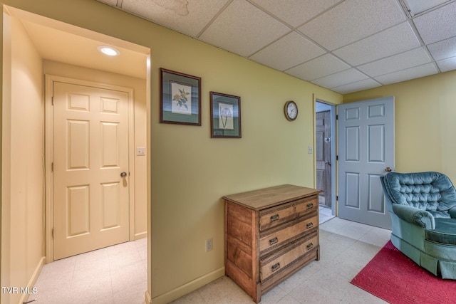 living area with a drop ceiling, baseboards, and light floors