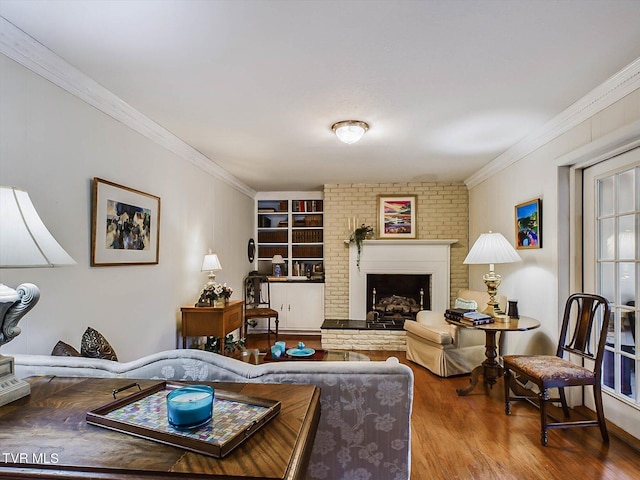 living room featuring built in shelves, crown molding, wood-type flooring, and a brick fireplace