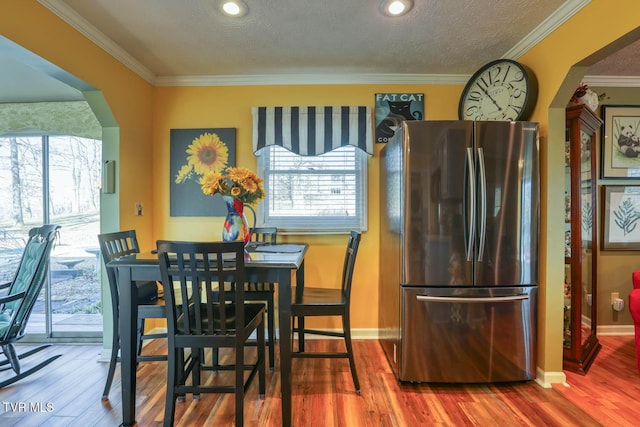 dining space with wood-type flooring, ornamental molding, and a textured ceiling