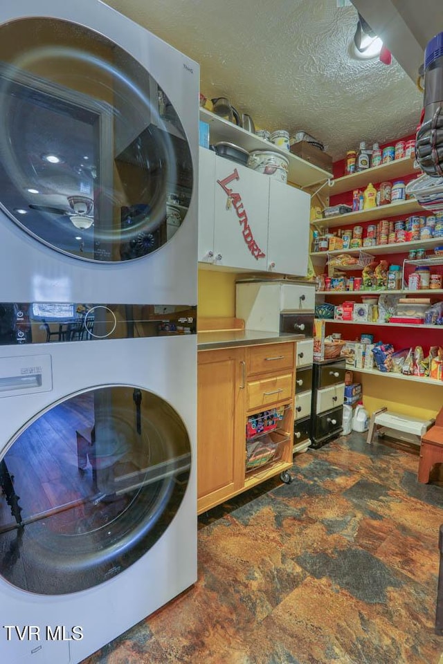 laundry area featuring stacked washer / dryer, cabinets, and a textured ceiling