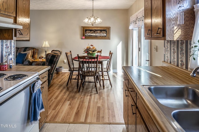 kitchen featuring pendant lighting, electric stove, sink, light hardwood / wood-style flooring, and a notable chandelier