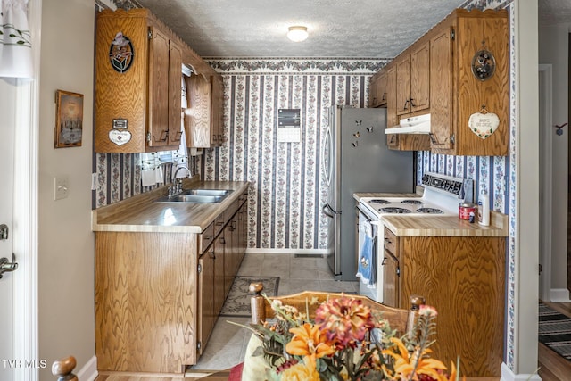 kitchen with sink, light tile patterned floors, a textured ceiling, white range with electric stovetop, and stainless steel refrigerator