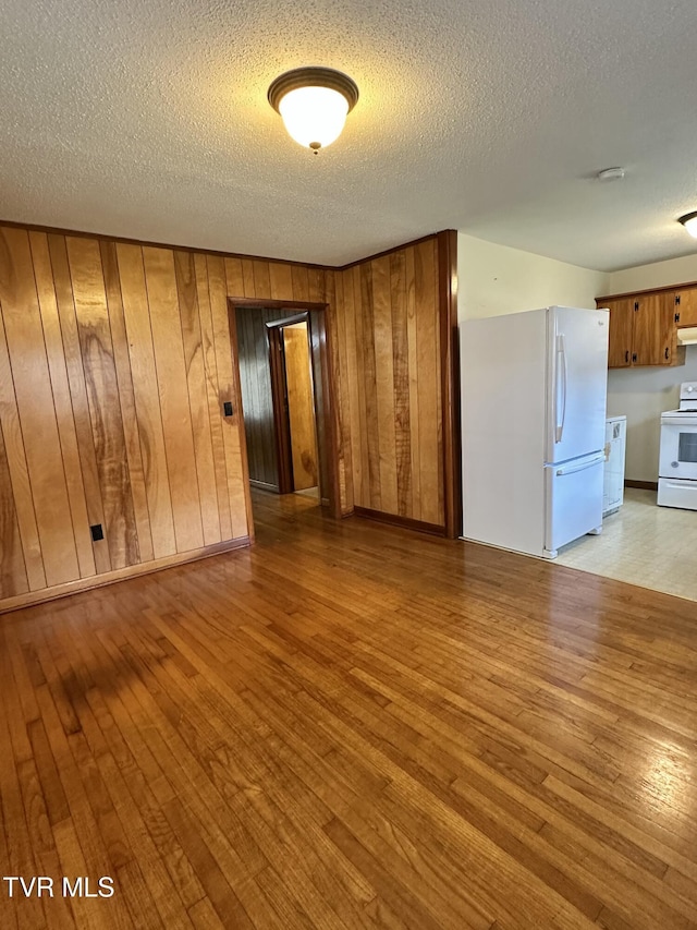 spare room featuring wooden walls, light hardwood / wood-style flooring, and a textured ceiling