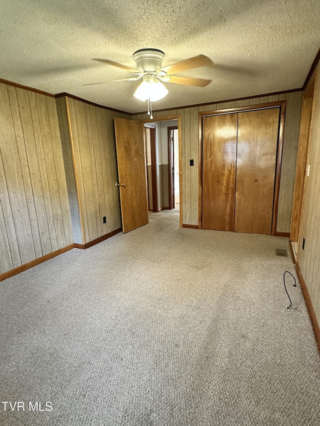 unfurnished bedroom with light carpet, ceiling fan, and wood walls