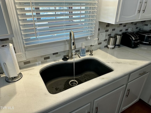 interior space with backsplash, white cabinets, and sink