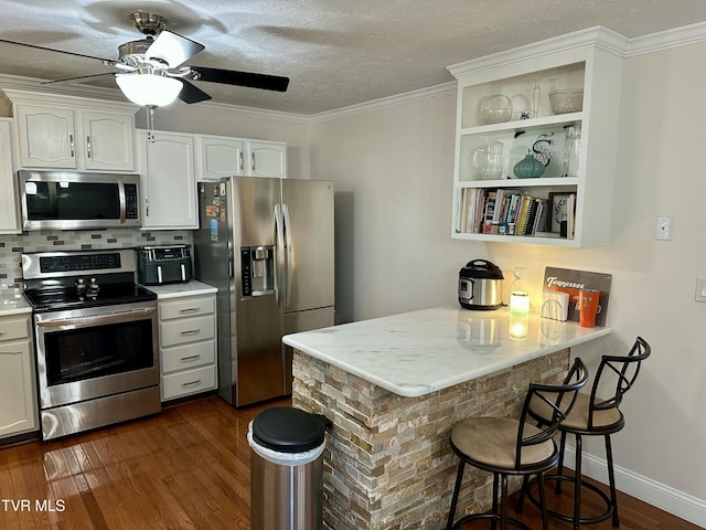 kitchen featuring white cabinetry, stainless steel appliances, a kitchen breakfast bar, dark hardwood / wood-style flooring, and kitchen peninsula