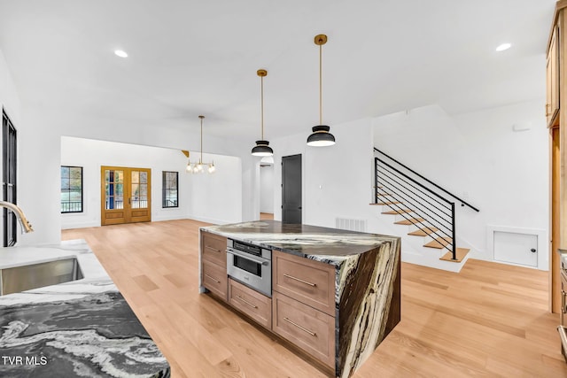 kitchen with sink, stainless steel oven, french doors, dark stone countertops, and light wood-type flooring