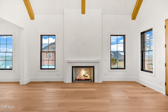 unfurnished living room featuring beam ceiling, light hardwood / wood-style floors, and plenty of natural light