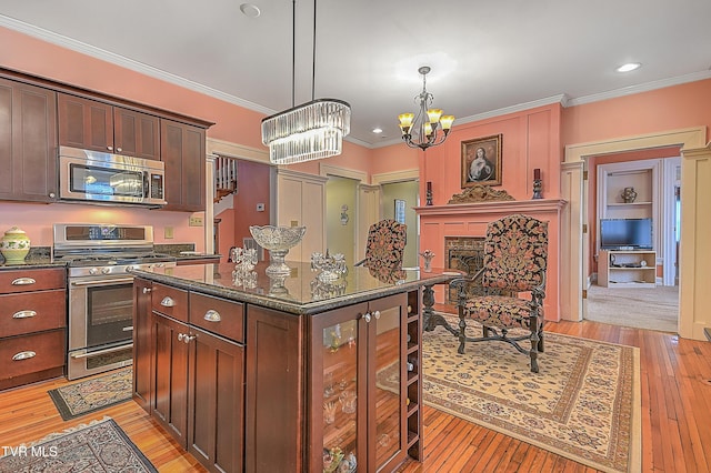 kitchen featuring appliances with stainless steel finishes, decorative light fixtures, dark stone countertops, crown molding, and light wood-type flooring