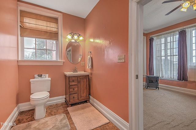 bathroom featuring vanity, ceiling fan, toilet, and a wood stove