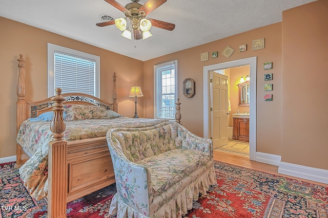 bedroom featuring ceiling fan, ensuite bath, wood-type flooring, and a textured ceiling