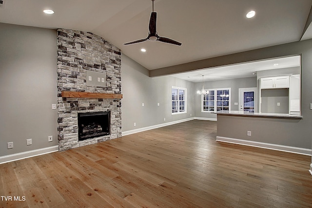 unfurnished living room with lofted ceiling, a stone fireplace, ceiling fan with notable chandelier, and hardwood / wood-style flooring